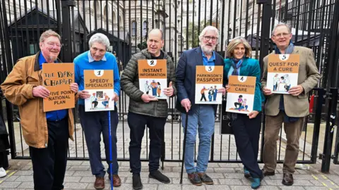 PA Media Hosts of The Movers and Shakers podcast (left-right) Mark Mardell, Paul Mayhew-Archer, Rory Cellan-Jones, Jeremy Paxman, Gillian Lacey-Solymar and Sir Nicholas Mostyn, mark World Parkinson's Day by handing in their 'Parky Charter' petition to Downing Street