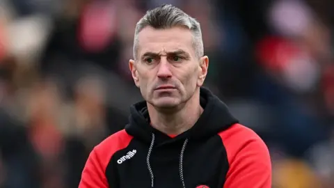 Getty Images Rory Gallagher on the side lines of a Derry football match in March 2023. He had grey, short hair and is wearing a black hooded top with red sleeves.