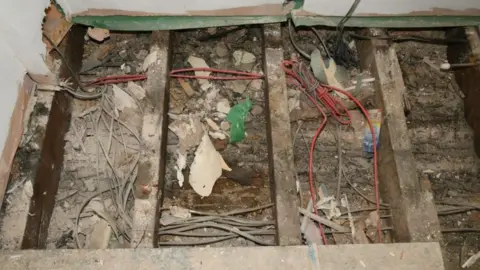 Durham Police An exposed area of floor from where the boards have been removed. It is a cluttered mess with fragments of wood and plaster having fallen into the whole between the wooden bars supporting the floor. There is also red wiring, but amid the mess is a section where there is a clear patch where presumably the baby was