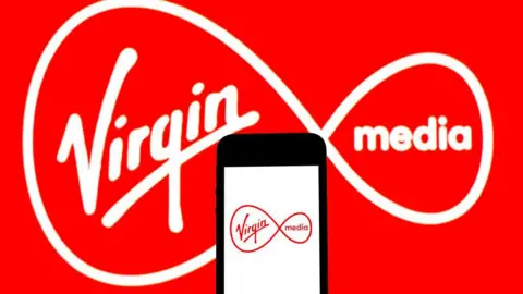 Virgin Media logo displayed on a smartphone against the company's red and white logo in the background.