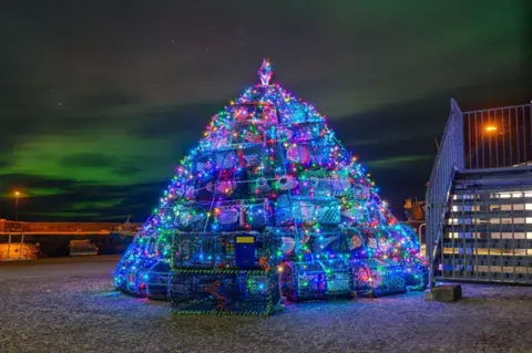 John Cumming Lobster pots arranged in a pyramid shape, decorated with lights to look like a Christmas tree.