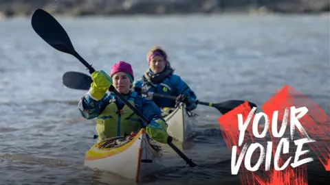 Getty Images Two women in kayaks, wrapped up against the elements. A Your Voice logo is in the bottom right hand corner of the picture. 