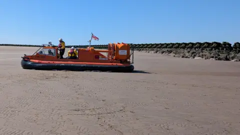 RNLI Hoylake's hovercraft on New Brighton beach on a sunny day as the Coastguard and RNLI rescue a woman. 