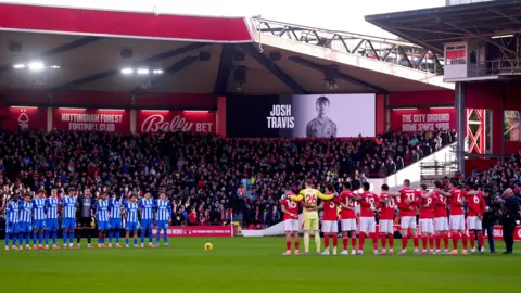 Pail Media Players and fans playing on the ground of the city in Untingham stand in silence before going to the Forest Forest on November 30, 2025 in the Joshon mekanan. A black and white image of a teenager appeared on the screen that was left standing. 