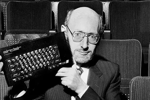 Getty Images A man in his 40s with glasses and a suit holds up a small personal computer