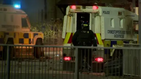 Officer in riot gear next to PSNI land rovers