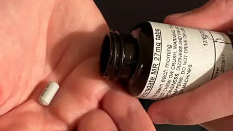 A pill in the palm of a hand with an open medicine bottle in the other hand