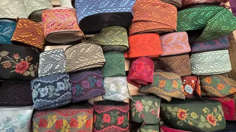 A tray of brightly coloured silk ribbons with flower designs and leaves on them.