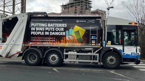 A rubbish truck with a poster on its side that says: "putting batteries in bins puts our people in danger."
