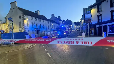 Antrim Arms hotel pictured behind a red and white fire and rescue service tape that says do not cross. There is a fire engine in front of the building.