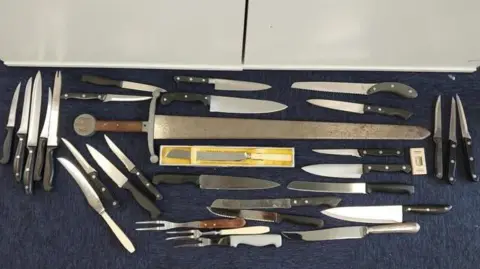 Knives, carving forks and a sword laid out on the floor of a police station