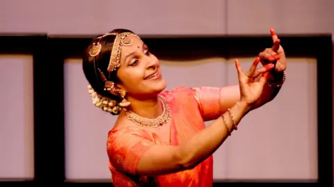 Krishna is dancing in traditional South Asian red / orange dress.