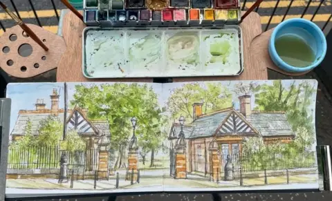 Allan Richardson A watercolour painting of the entrance to Glasgow's Botanic Gardens. The painting is in a sketchbook and sat on an easel with paintbrushes, a water pot and a paint palette.