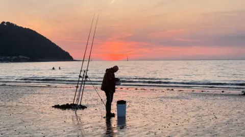 WeatherWatchers/Sparky A fisherman with his rods dug into the sand, standing in front of the tide