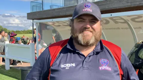 Jack Maclean/BBC Anglian Vipers chairman Rob Humphries poses by the dugout, wearing a Vipers-branded hat and some coaching kit