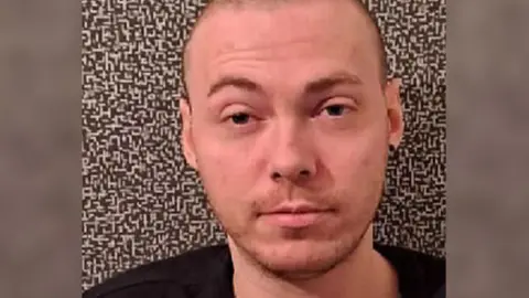 Police Scotland Grant McKinnon is looking straight at the camera. He has a shaved head and is wearing a black top