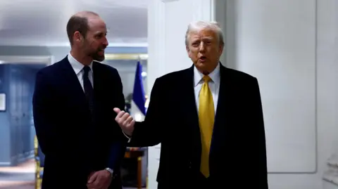 Reuters Prince William, dressed in a dark suit and tie, speaks with Donald Trump, who wears a black suit, white shirt, and yellow tie.