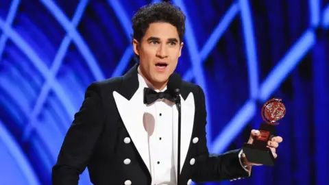Reuters Darren Criss accepts Best Performance by an Actor in a Leading Role in a Musical award for "Maybe Happy Ending" at the 78th Annual Tony Awards in New York City. He is wearing a black jacket with white lapels and white buttons.
