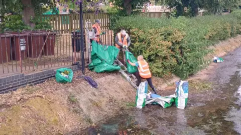 Syston Community Flood Group Volunteers moving bags of gathered waste up a ladder placed on the bank