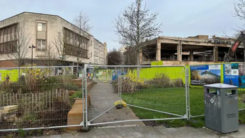 Construction site fencing set up to block off a path and some planted areas
