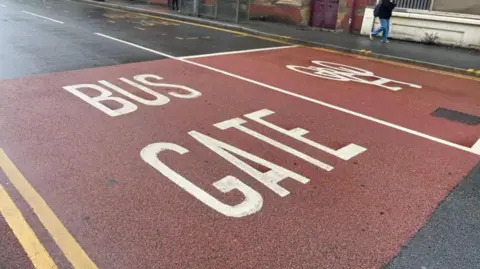 A road which has red paint on and the words Bus Gate in white. There are also double yellow lines. 