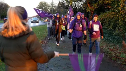 Dundee and Angus College staff and students waving purple flags, walking along a pavement.