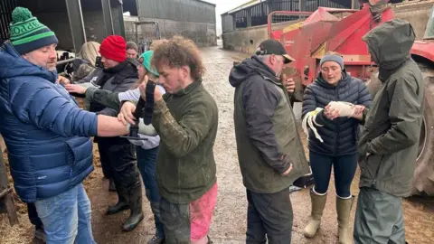 A group of farmers being delivered first aid training by the charity F3A. The group of men and women are standing in a farm yard demonstrating techniques such as using bandages and other strapping