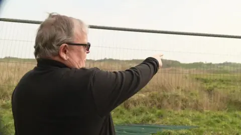 A man is turned away from the camera and pointing towards a field in the distance