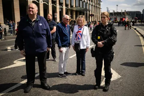 Leon Neal/Getty Images A police officer (R) stands with members of the public as they observe the two-minute silence near Parliament Square on May 08, 2025 in London, England.