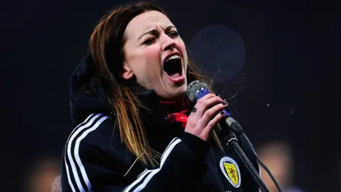 Getty Images Amy Macdonald singing at Hampden Park, wearing a tracksuit with the Scotland logo on it