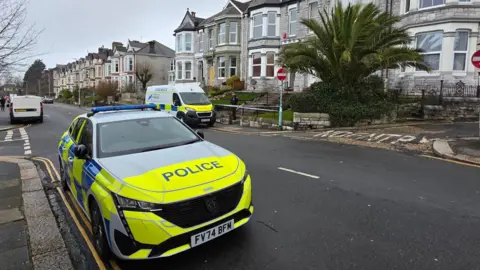 Two police cars and a tape cordon at a property on Lipson Road, in Plymouth