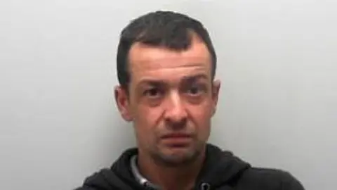 Custody picture of a man with short dark hair in a black hoodie.