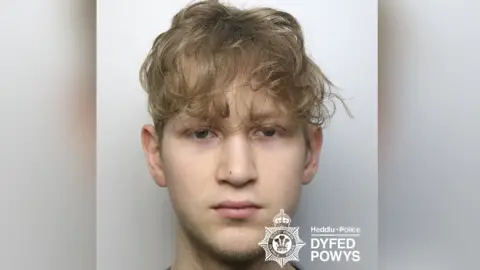 A young man is pictured with blonde hair looking at the camera