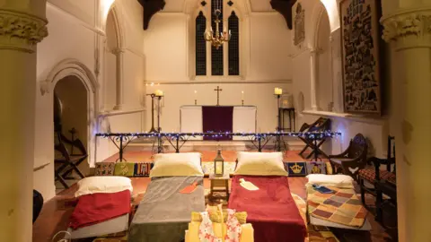 National Churches Trust Four single beds set up in a church with an alter behind them.