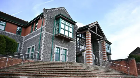 The outside of Canterbury crown Court. The image is taken from close to the ground at the bottom of a set of steps leading to a large grey brick building