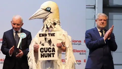 EPA Angus Robertson, with grey hair, claps next to a man dressed as a bird 