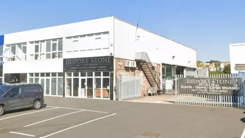 Google Bespoke Stone's workshop on Dales Road, Ipswich. It is a white building with a warehouse at the back. A car park is at the front of the building