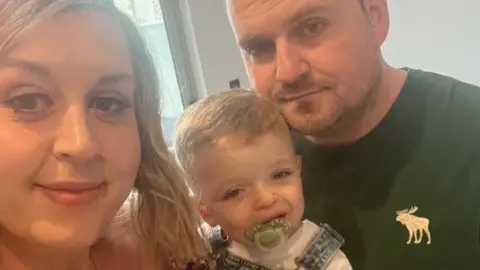 Lydia Collins Lydia Collins with light shoulder-length hair, holding her son, wearing dungarees and sucking a dummy, next to Ben Link, who is wearing a dark sweatshirt