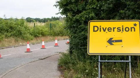 Yellow diversion road sign to the right with a line of traffic cones in the middle of a road to the left