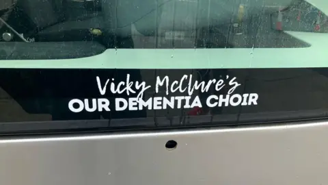 A close up of a tram window with signage that reads 'Vicky McClure's Our Dementia Choir'