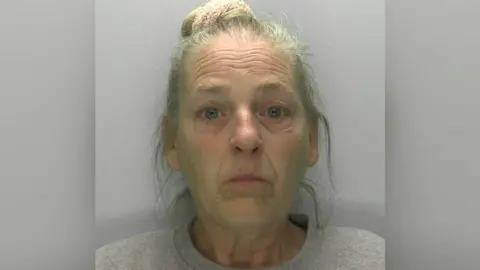 Mug shot of Donna Green. She has her grey hair up in a bun and is wearing a grey shirt. 