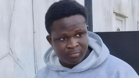 Miracle Oladoyinbo wearing a grey hoodie with white patterns on the front.