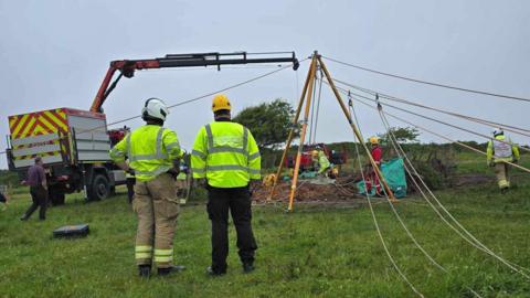 Several fire fighters in a field using specialist lifting equipment.