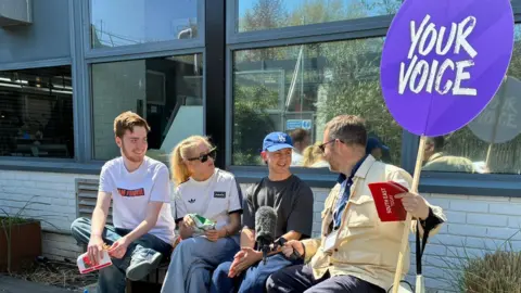 Left to right Samuel Wheatley, 21, Caitlin Noyce, 21, Taylor Jordan, 20, who are all graphics students are interviewed by BBC South East tody reporter, Peter Whittlsea. He holds a Your Voice sign.