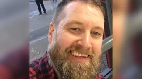 LDRS A selfie shot of Chris Evans with a heavy beard, wearing a cotton red and black check shirt 