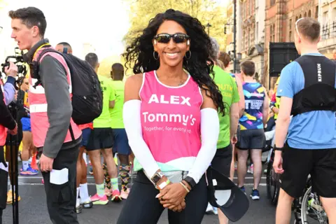 PA Media Alexandra Burke standing among other runners wearing sunglasses and a pink running top