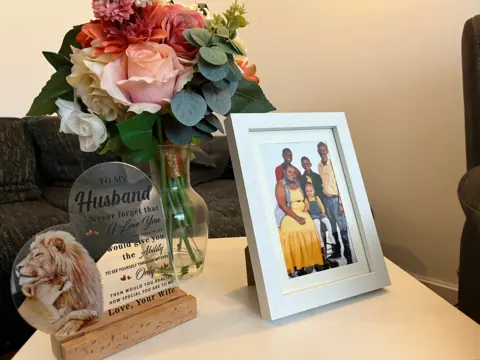 A framed photo of the family along with a plaque and a bunch of flowers.