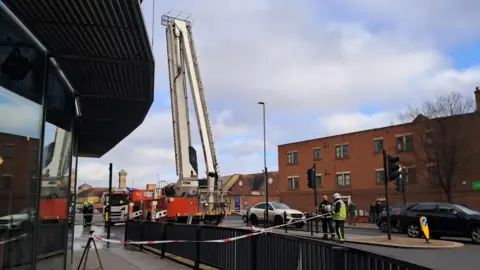 A fire engine and a cherry-picker parked outside Stockton Arc. Firefighters have cordoned off the road outside using red and white tape.