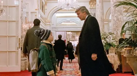 20th Century Fox / Alamy Screenshot from Home Alone 2, where Kevin, played by Macaulay Culkin, bumps into Donald Trump in the lobby of the Plaza Hotel
