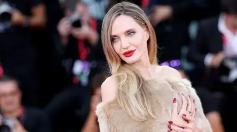 Getty Images Angelina Jolie wearing a faux fur dress against a backdrop of photographers